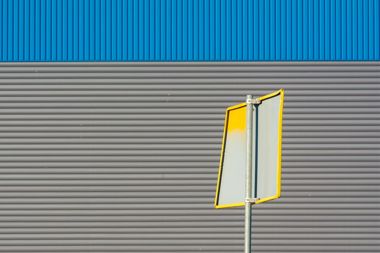A yellow-bordered signpost against a corrugated gray wall with blue accents.